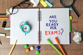 Notebook open that says are you ready for exams. There are pens, paper clips, eye glasses, magnifying glass and crumpled papers.